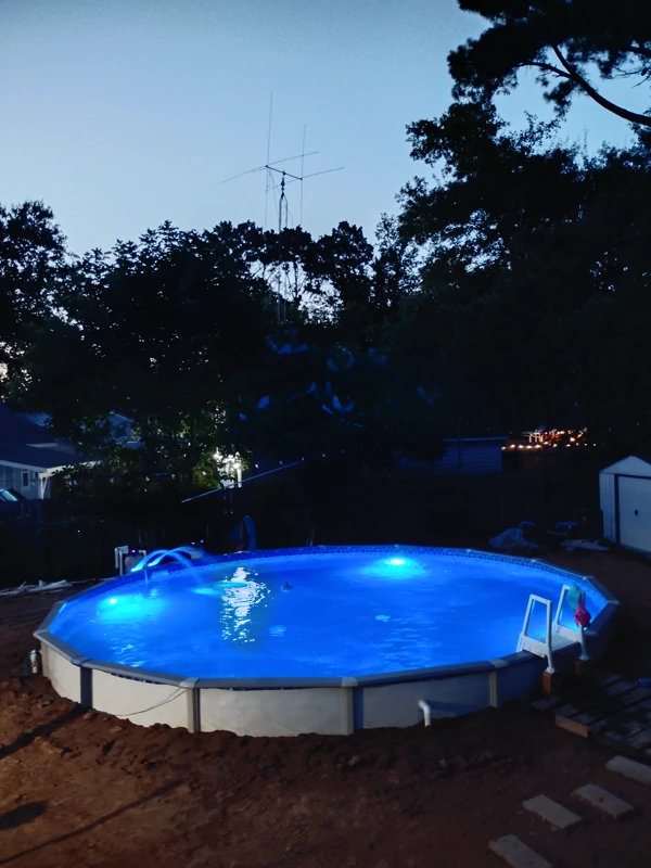 Above-ground pool lit at night beside a deck