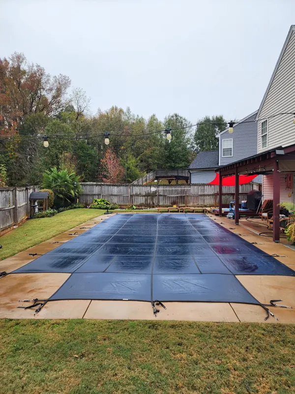 Mesh safety cover on a rectangular pool beside a house